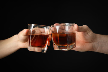 Male hands holds glasses of whiskey on black background, close up. Cheers