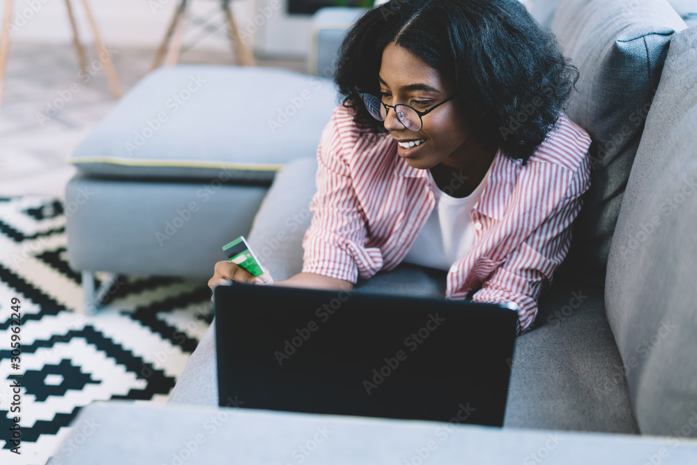 Poster smiling dark skinned hipster blogger looking at credit number of plastic card to make money transact
