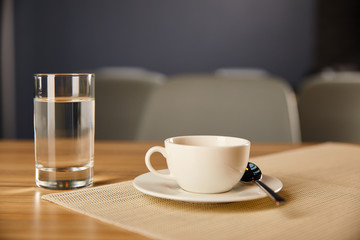 selective focus of cup of coffee near glass with water in cafe