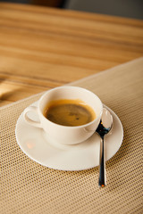 selective focus of cup with hot coffee near spoon in cafe