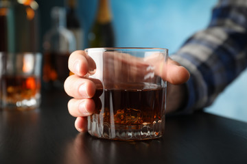 Male hand holds glass of whiskey on black table, close up