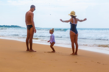 happy family, mom dad and little daughter on the shore of the sandy beach by ocean spend time and walk.