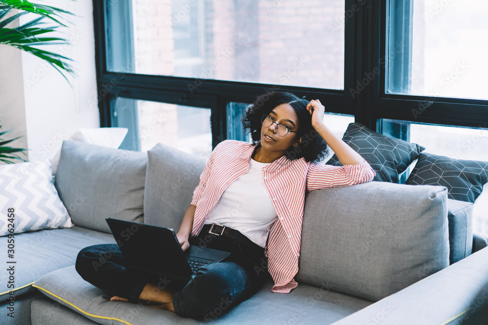 Poster pondering african american young woman relaxing on comfortable couch and thinking on development of 