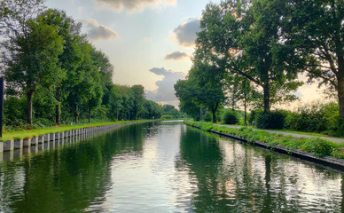 Beautiful and dramatic sunset or sunrise with colorful clouds and light rays in the sky over the river or canal with reflections on the water 