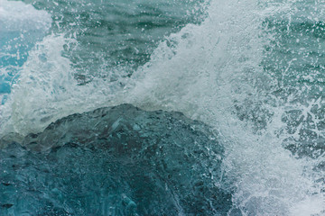 Obraz premium Wave water splash crushing into clear iceberg on the beach Antarctice