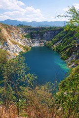 Beautiful scenic of a mining quarry with a waterlogging area in the middle against the mountain and blue sky background which is a tourist attraction in Chon Buri, Thailand