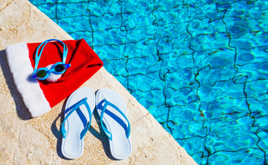 Flip flops and swimming goggles near the pool, Santa Claus hat, Christmas vacation, sandals and swimming glasses by water, slippers and pool goggles near swimming pool