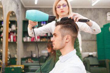 Hairdresser dries hair of stylish man.  Young handsome guy doing hair styling at a hairdresser