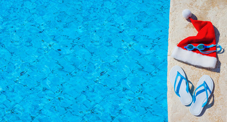Flip flops and swimming goggles near the pool, Santa Claus hat, Christmas vacation, sandals and swimming glasses by water, slippers and pool goggles near swimming pool