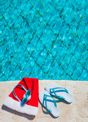 Flip flops and swimming goggles near the pool, Santa Claus hat, Christmas vacation, sandals and...