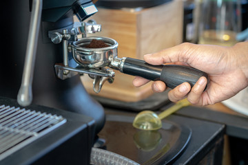 Action photo of coffee shop's barista is operating the coffee bean grinder machine, taking a filter block to receive it. Close up and selective focus.