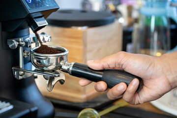 Action photo of coffee shop's barista is operating the coffee bean grinder machine, taking a filter block to receive it. Close up and selective focus.