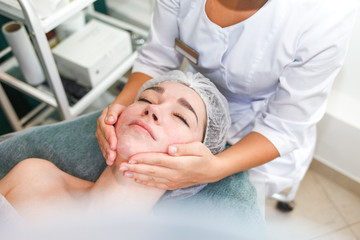 Doctor beautician makes cosmetic facial massage. Woman relaxes on a cosmetic chair
