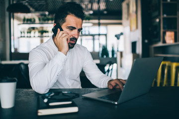 Skilled male entrepreneur reading received email with week schedule information and calling to personal secretary for discussing details, man working remotely with laptop using cell for phoning