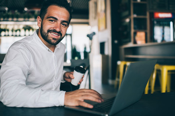 Portrait of happy male entrepreneur working remotely in public coffee shop with high speed internet connection, skilled successful man using laptop application for accounting online document