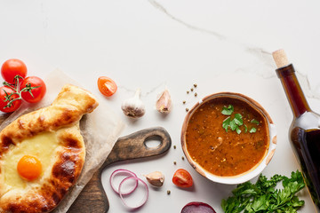 Top view of adjarian khachapuri, soup kharcho, wine bottle and vegetables on marble texture