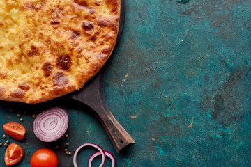 Top view of imereti khachapuri with vegetables on textured green background