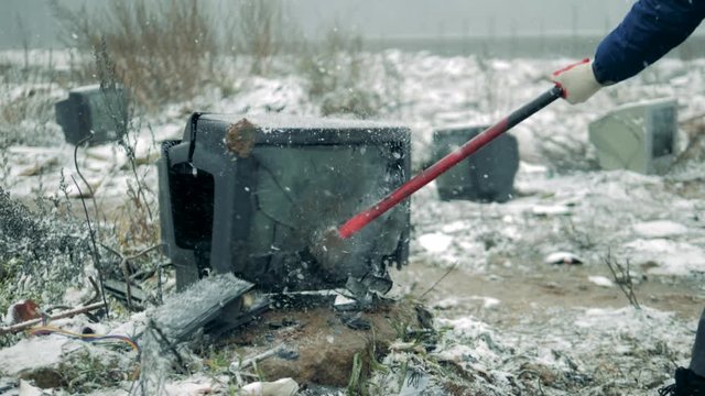 Person breaks a TV with a hammer at a dump. Man with a hammer shatters the TV screen.