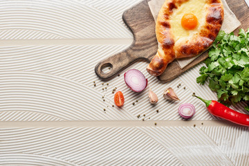 Top view of adjarian khachapuri with vegetables and cilantro on textured background