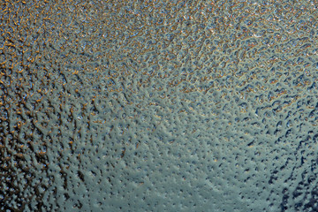 A blue-green surface of mercury-like ice. Hue jade or ultramarine. Abstract winter background or wallpaper. Cold and frost. Close-up