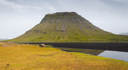 Tall table mountain by the meadows and river with black sand, Iceland Kirkjufell 