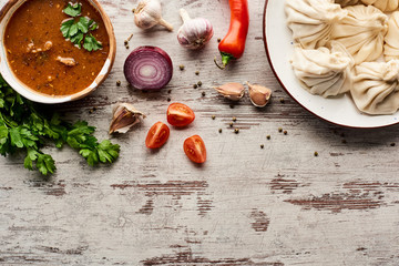 top view of delicious khinkali and kharcho near vegetables and spices on wooden table with copy space