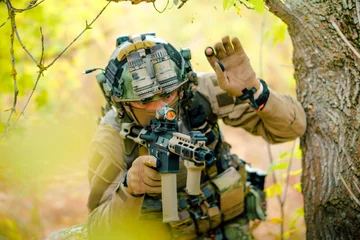 Tuinposter Closeup airsoft man in uniform with machine gun move through the forest. Soldier aims at the sight © Bohdan Petrushko
