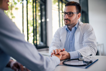 Friendly male doctor holding patient's hand for encouragement and empathy.