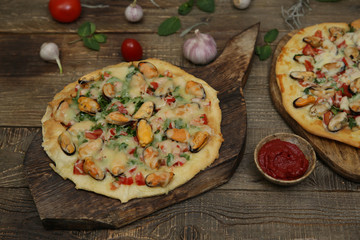 two seafood pizzas with mussels and mozzarella cheese isolated on a wooden board and on a wooden rustic table. Mediterranean food. Vegetarian. Top view. With copy space for text. 