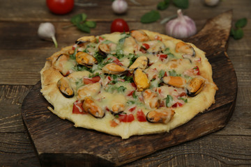 seafood pizza with mussels and mozzarella cheese isolated on a wooden board and on a wooden rustic table. Mediterranean food. Vegetarian. Close-up.