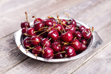 Fresh cherry in metal bowl on wooden background Retro style Close up