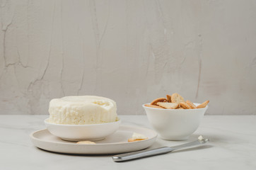 Cheese and cracker in a white bowl with a knife on a white background. Copyspace.