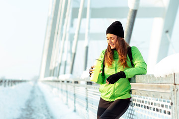 Young woman rest on the bridge and dring water afther jogging on snow