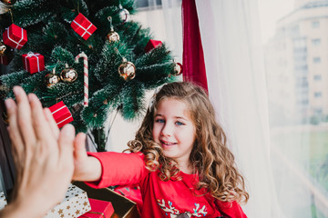 portrait of beautiful kid girl at home by the christmas tree. happy girl doing high five