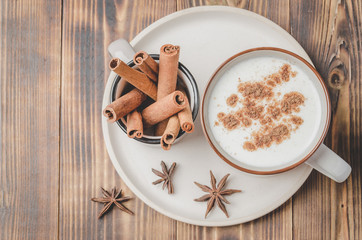 Eggnog. Traditional christmas cocktail in a mug and cinnamon sticks and anise on a white bowl on a wooden background. Top view.