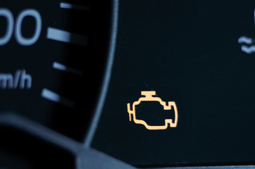 Yellow lit engine error sign on car dashboard close up