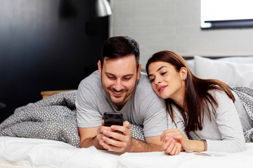 Young couple in bed looking on mobile phone
