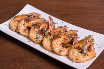 Spicy garlic chili prawns shrimps on white plate isolated over wooden background.