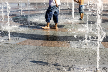 Children splashing in the city fountain. Hot summer day.