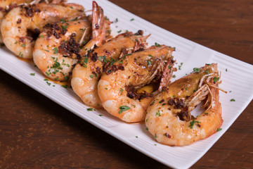 Spicy garlic chili prawns shrimps on white plate isolated over wooden background.