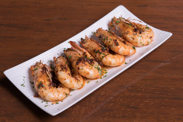Spicy garlic chili prawns shrimps on white plate isolated over wooden background.