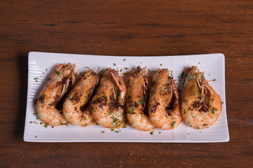 Spicy garlic chili prawns shrimps on white plate isolated over wooden background.