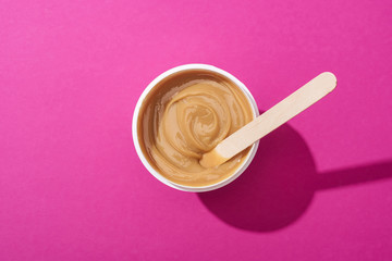 top view of depilation wax in cup with stick on pink background