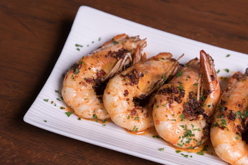 Spicy garlic chili prawns shrimps on white plate isolated over wooden background.
