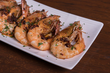 Spicy garlic chili prawns shrimps on white plate isolated over wooden background.