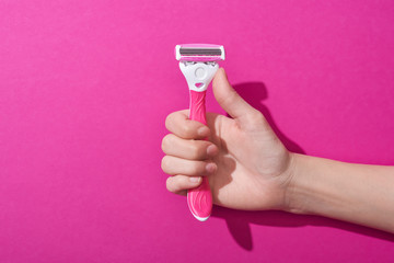 cropped view of woman holding razor on pink background