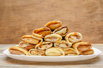 Pancakes with filling stacked pyramid on a white plate, standing on a wooden background close-up