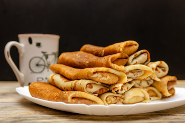 Homemade pancakes with filling stacked in a pyramid on a white plate against a black wall with a Cup, copy space