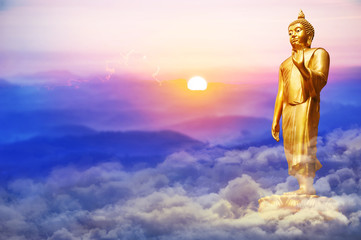 Golden Buddha statue standing on soft clouds field with   sunrise in the morning and mountain...
