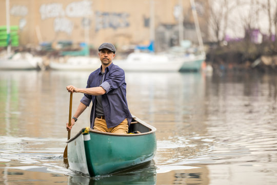 Man rowing a canoe in a river with a hat